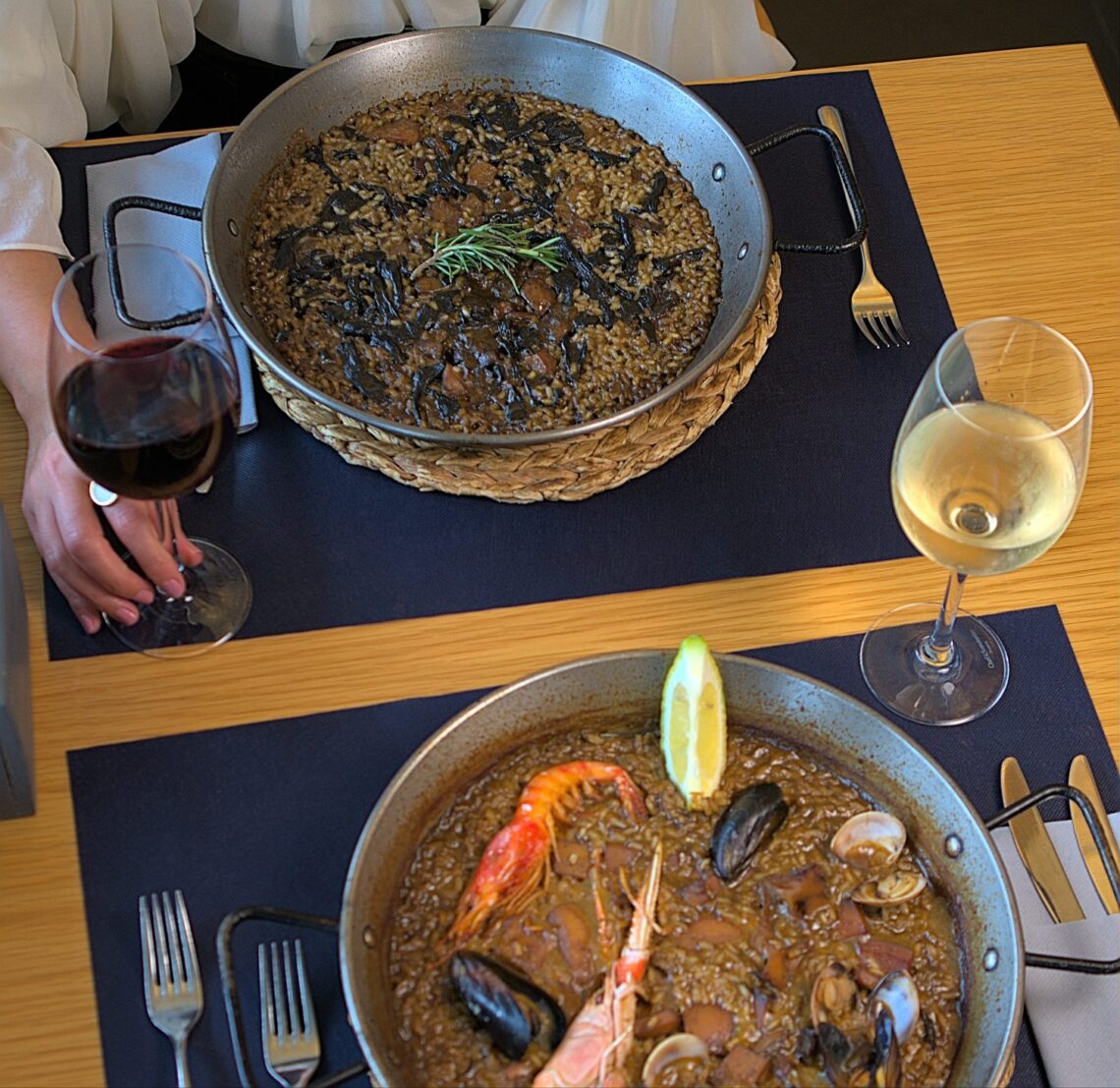 Paella garnie de fruits de mer servie avec des verres de vin blanc sur une table.