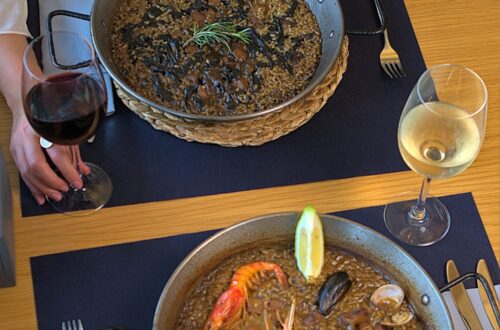 Paella garnie de fruits de mer servie avec des verres de vin blanc sur une table.